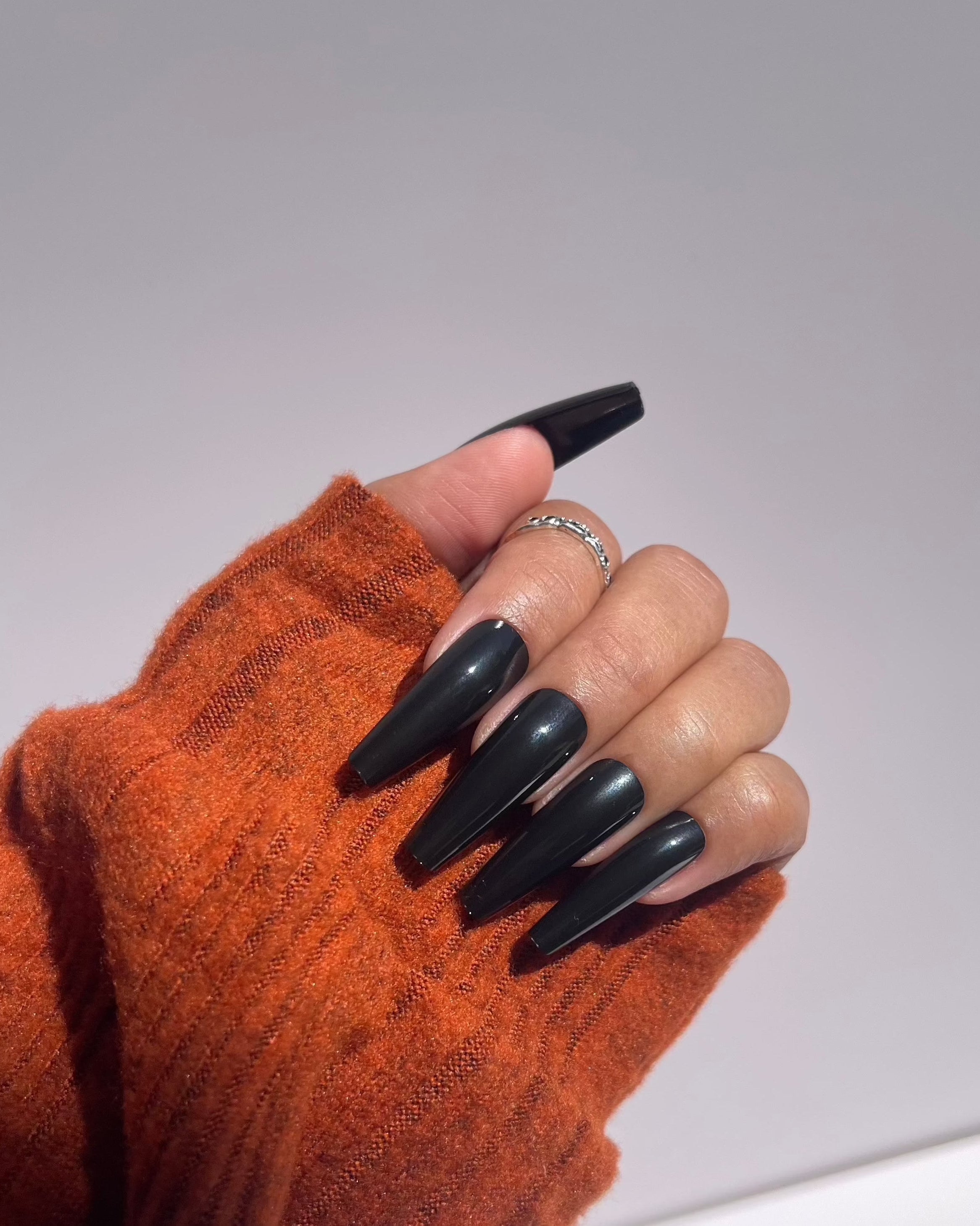 Glossy black press-on nails with orange sweater