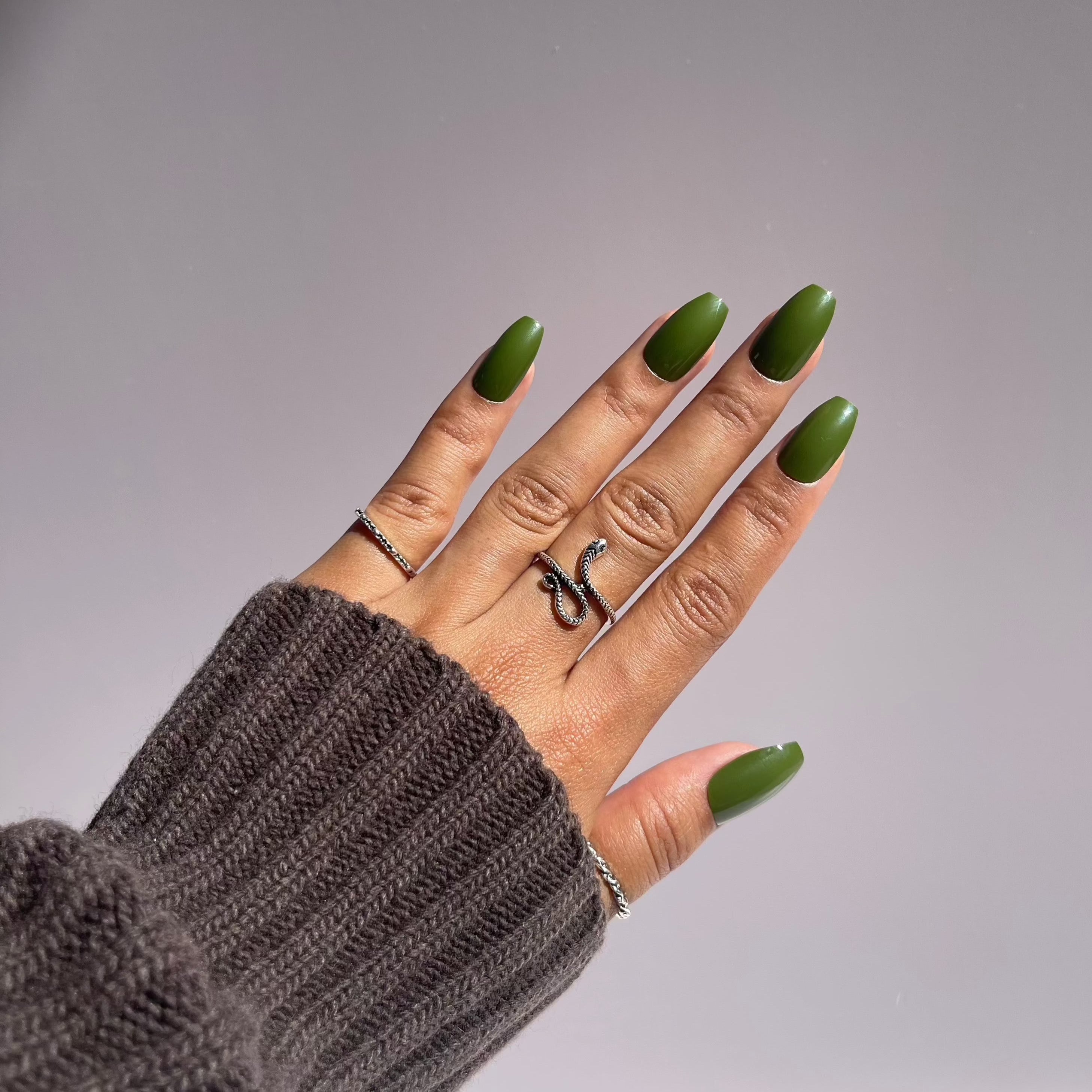 Hand with olive green press-on nails, cozy sweater.