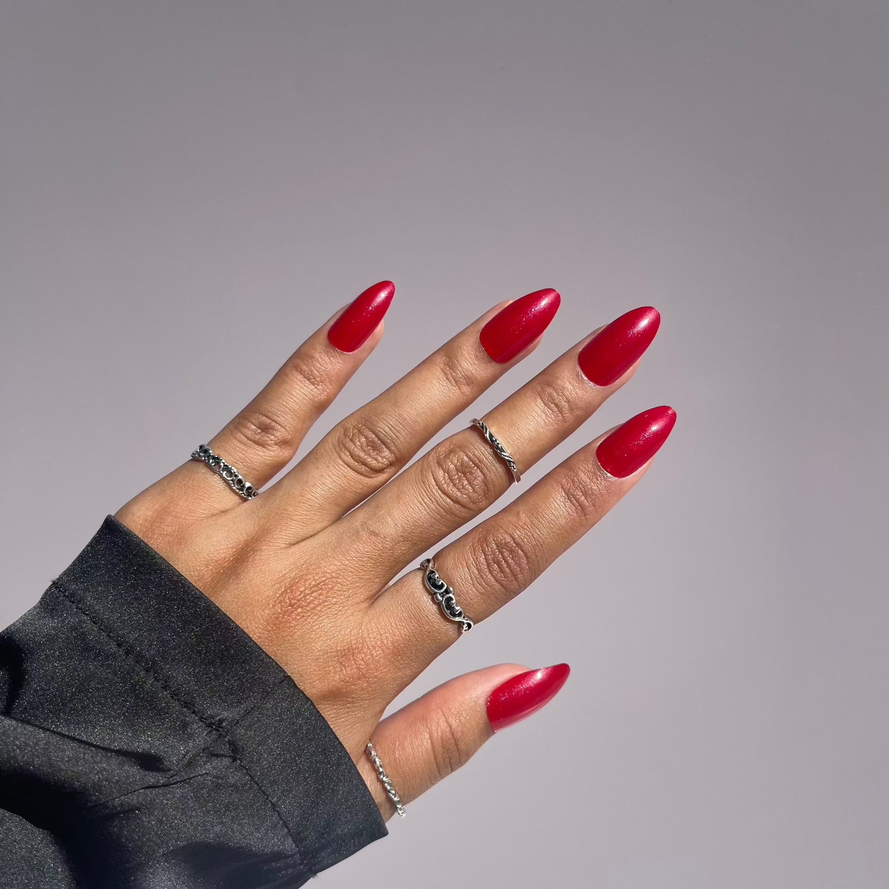 Red press-on nails with silver rings on hand