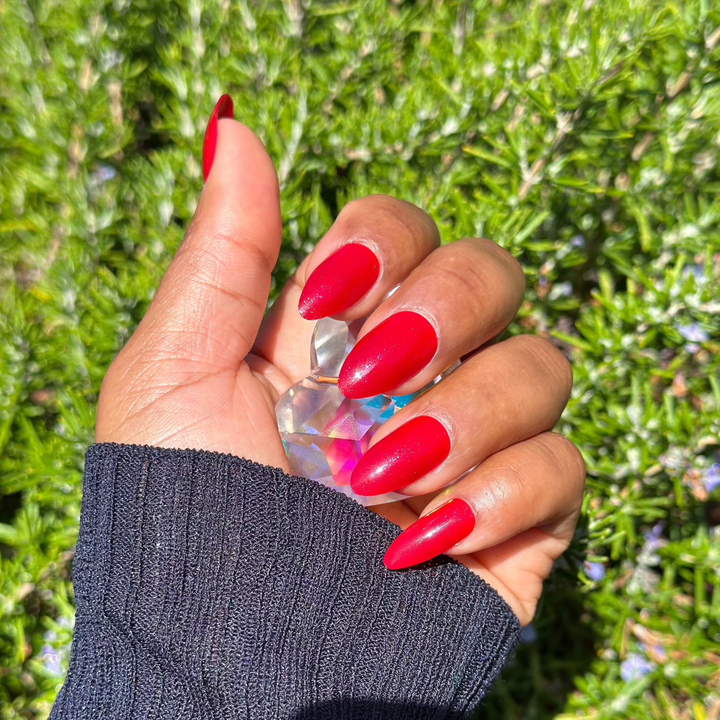 Red almond-shaped nails holding a crystal