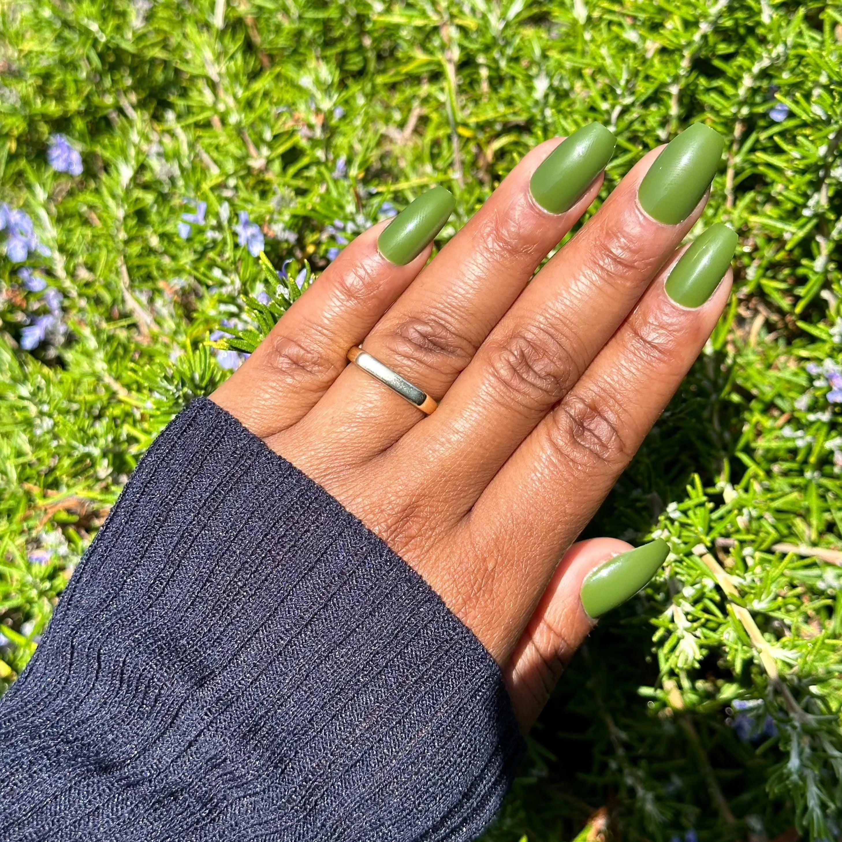 Hand with olive green nails against greenery background.