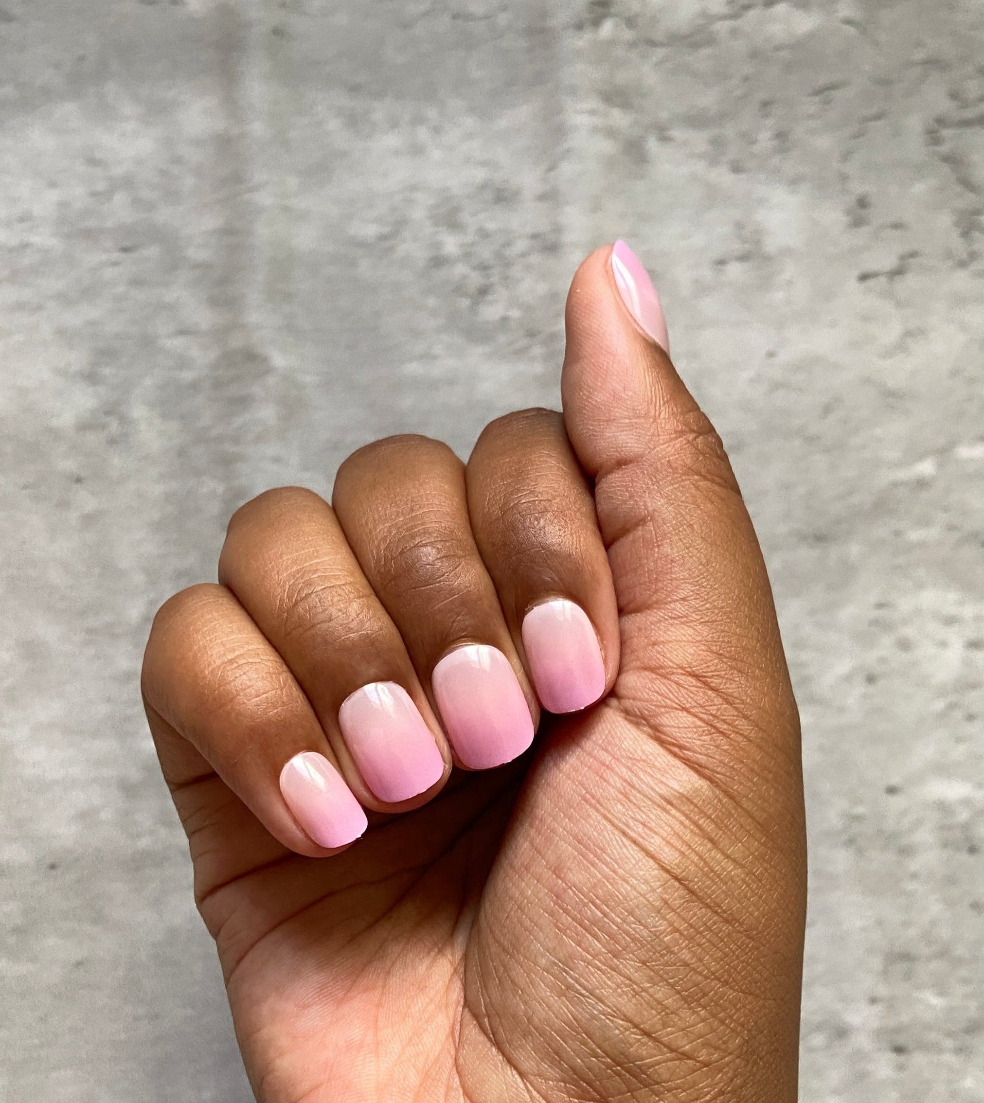 Hand with pink press-on nails and gold bracelet on a gray background