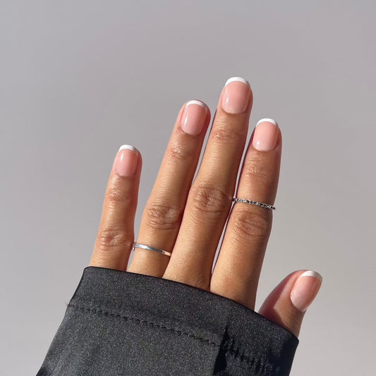 Hand with elegant French tip press-on nails and minimalist rings.