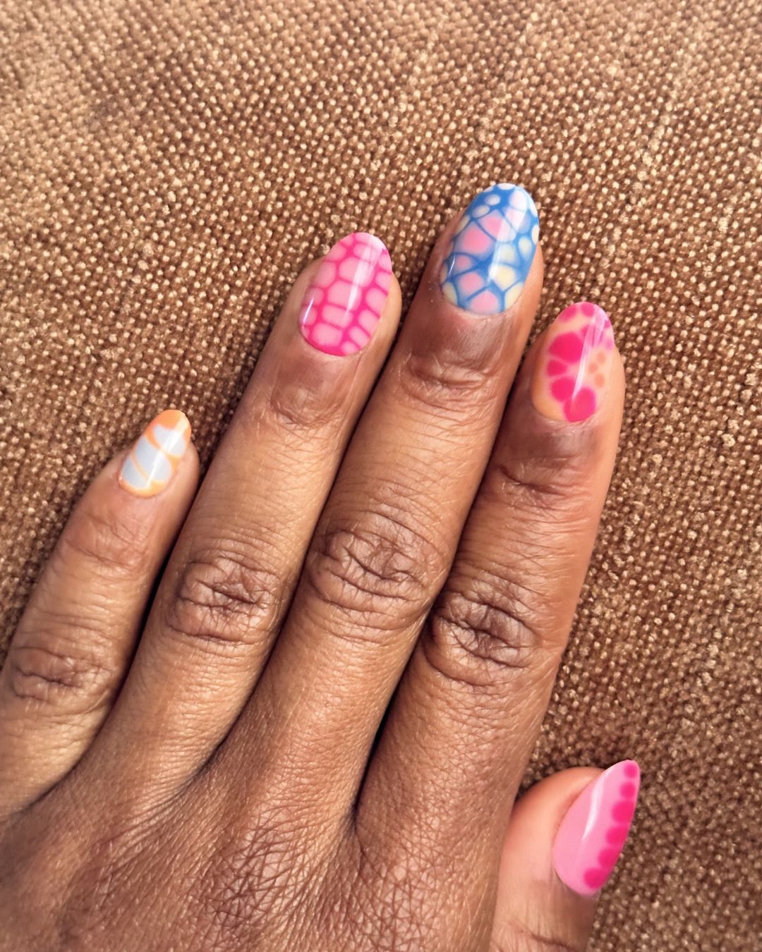 Hand with colorful nail art on a brown textured background