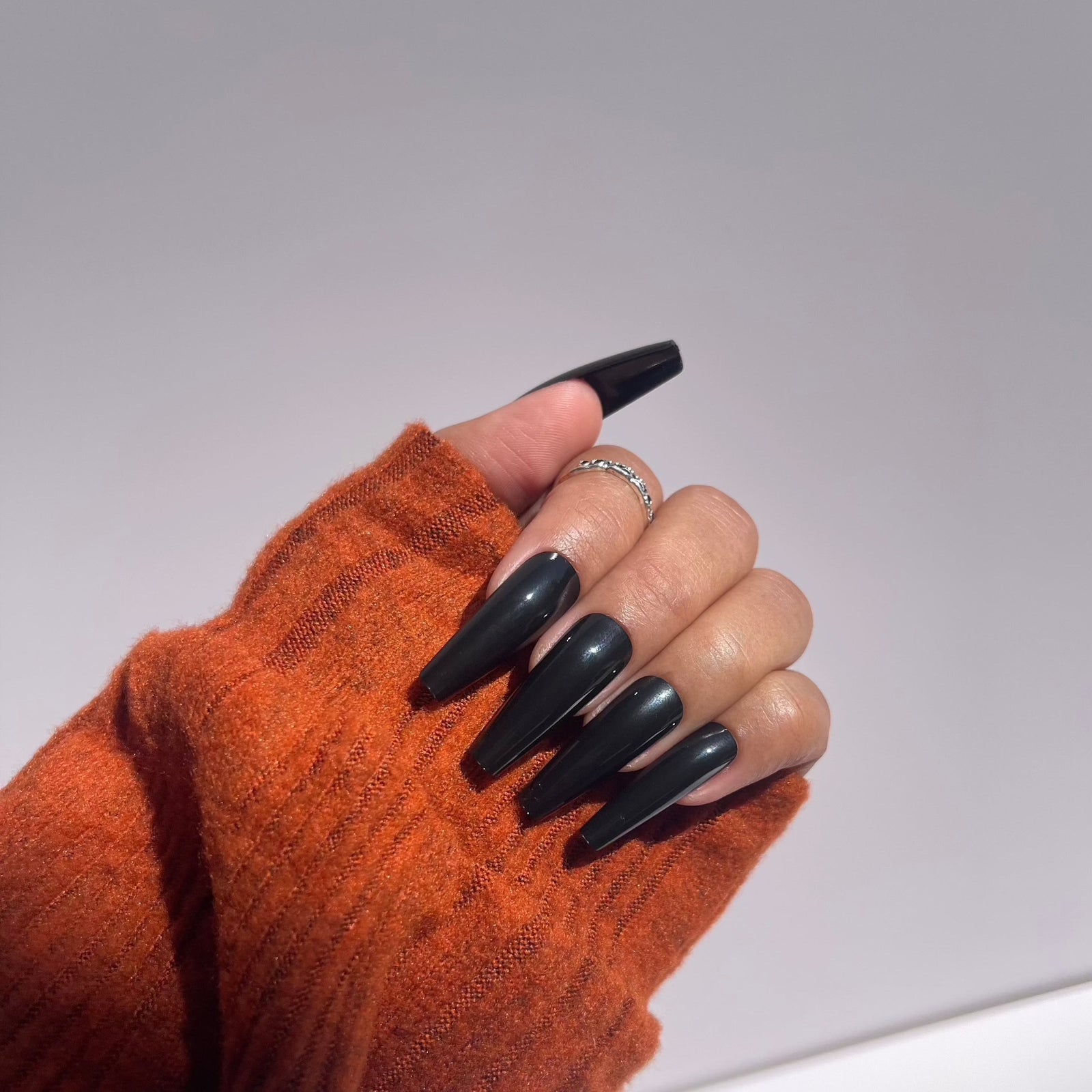 Glossy black press-on nails with orange sweater
