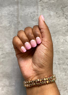 Hand with pink press-on nails and gold bracelet on a gray background