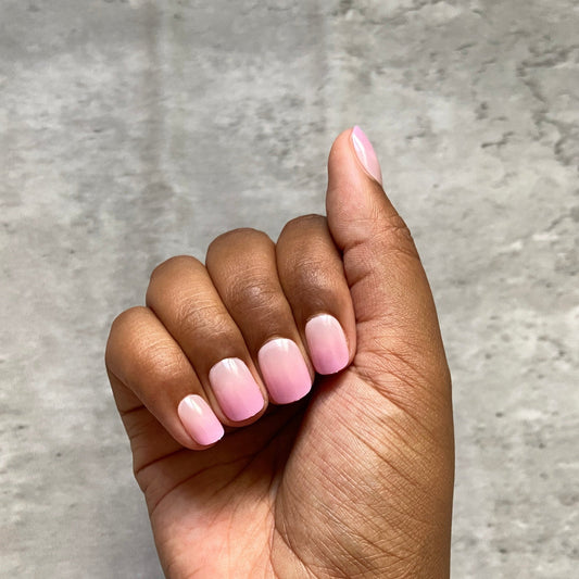 Hand with pink press-on nails and gold bracelet on a gray background