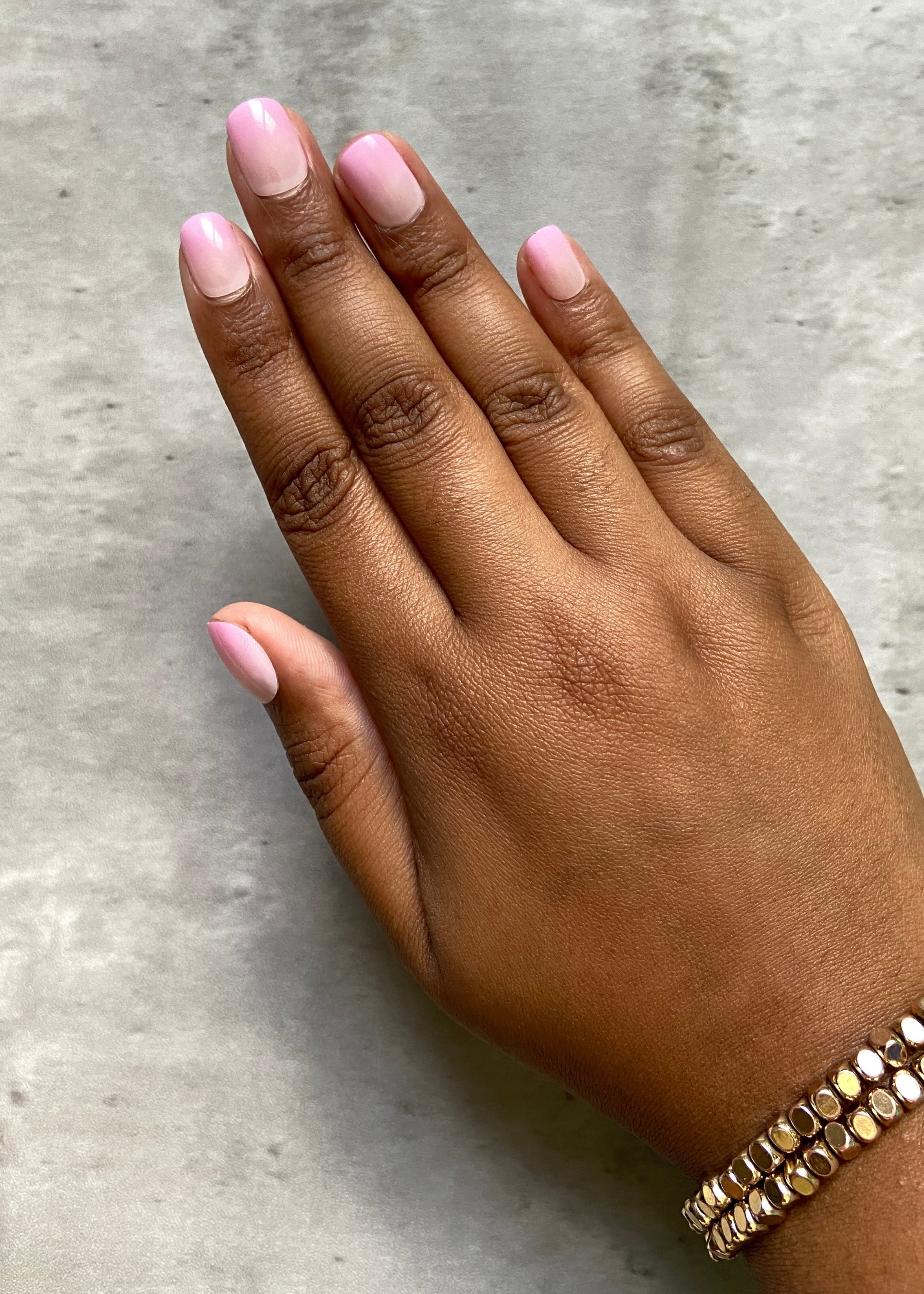 Hand with pink press-on nails and a gold bracelet on a gray concrete surface