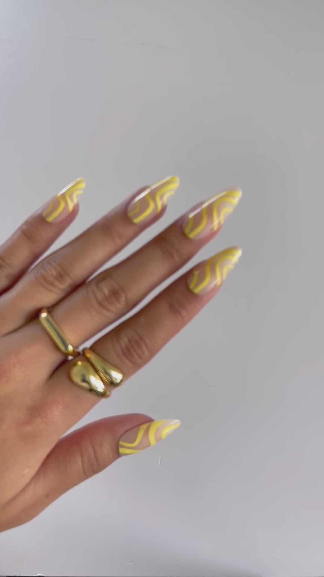 Close-up of yellow almond press-on nails with swirls