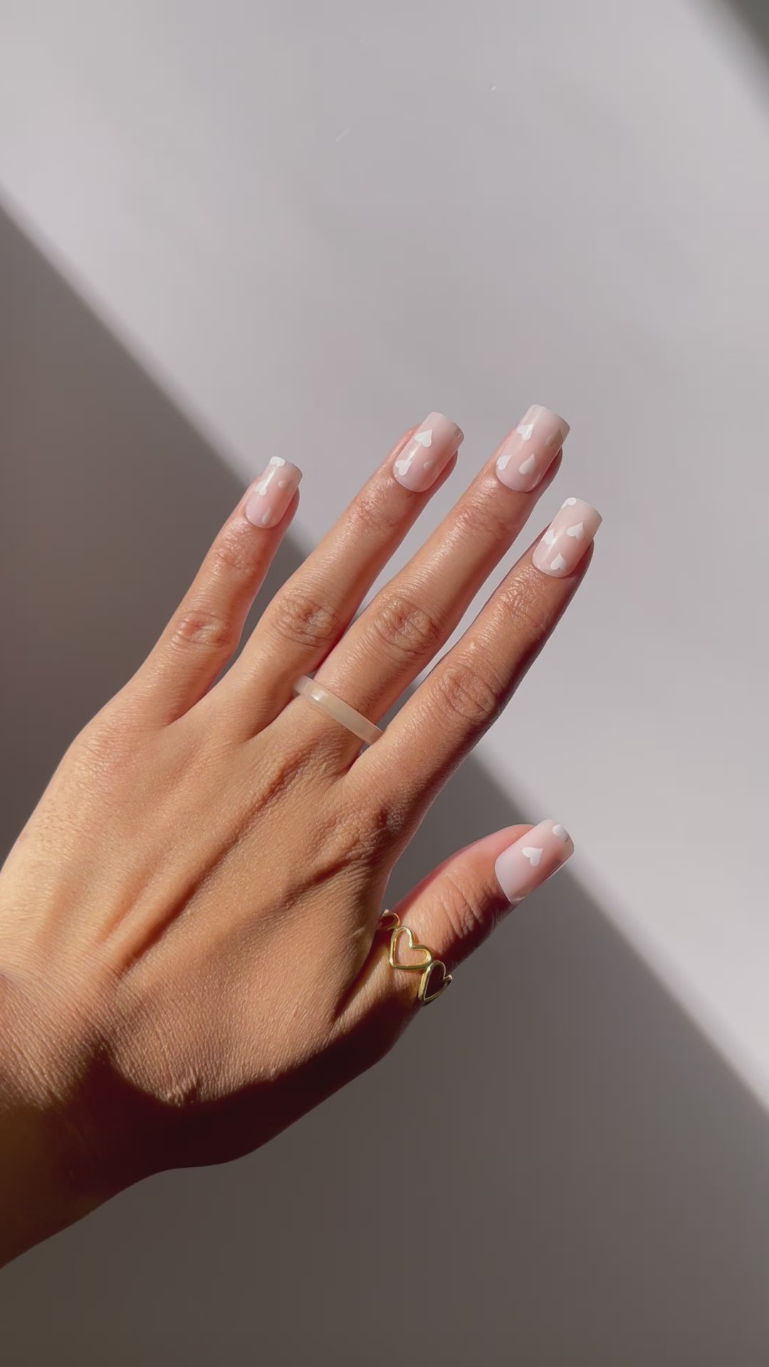 Short nude press-on nails featuring white hearts.